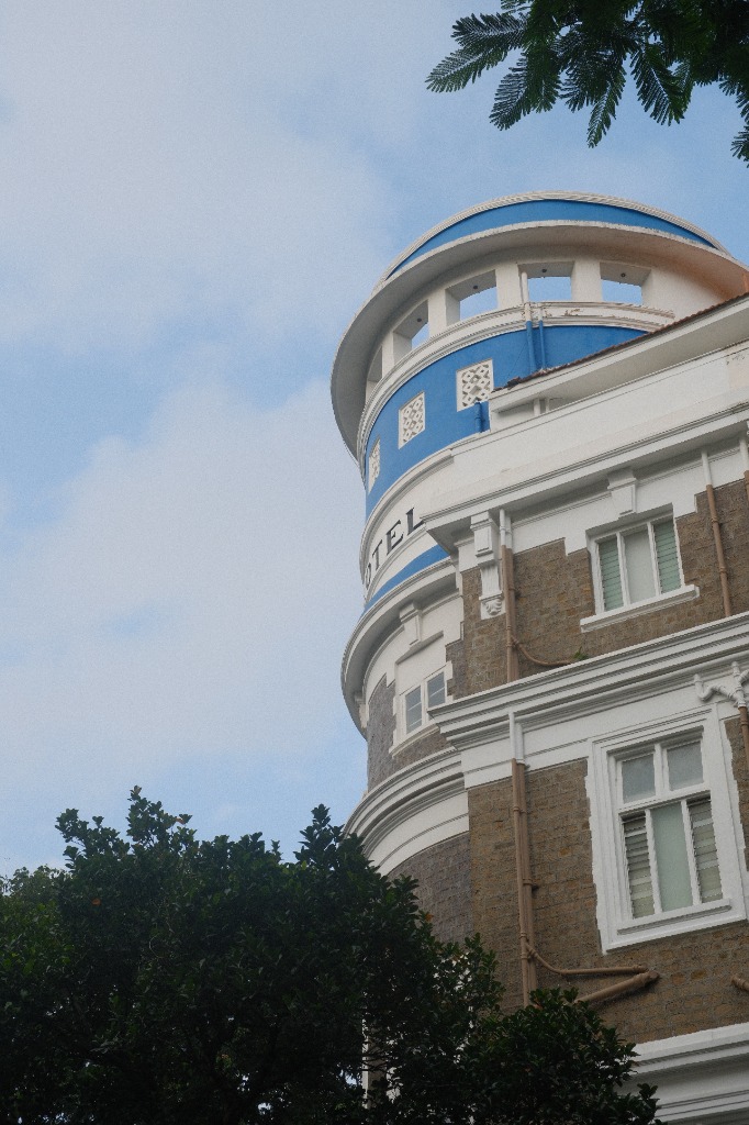 The curved blue-and-white corner tower of an Art Deco hotel against a pale, clouded sky
