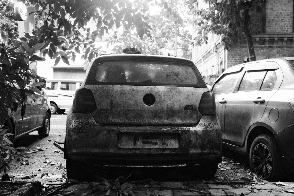 Gritty texture on a dirty car under tree foliage, demonstrating the sharp silver-halide-style grain structure.